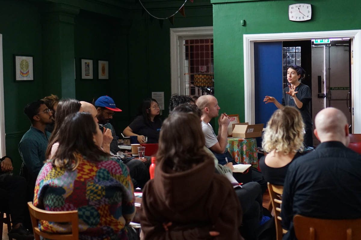 a diverse group of people sit listening to a woman talk.