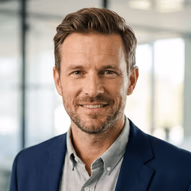 Ein lächelnder Mann im Anzug vor einem Bürohintergrund.