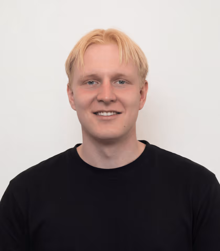 Lächelnder Mann mit blonden Haaren und schwarzem T-Shirt vor weißem Hintergrund.