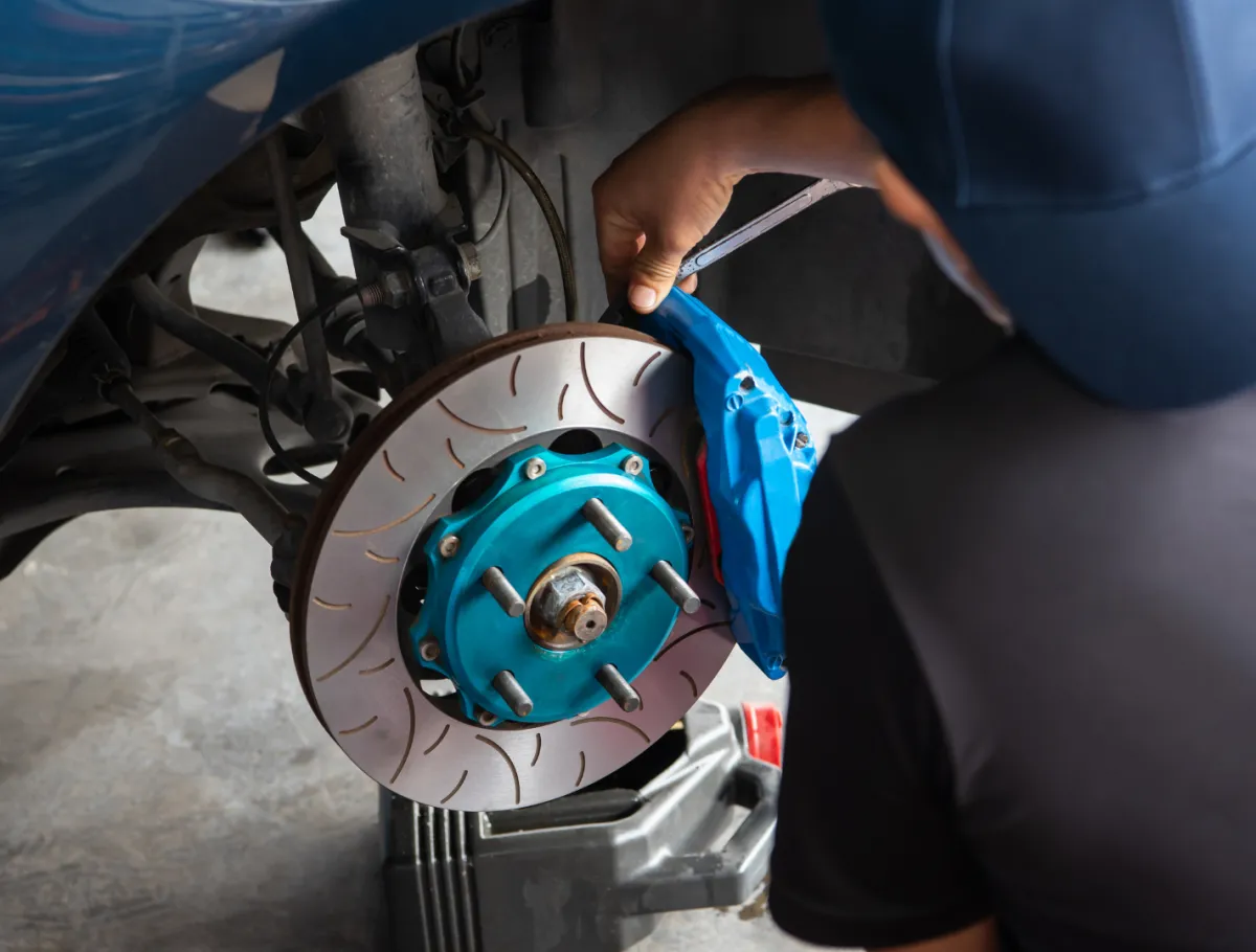 Mechanic tightening blue brake caliper on a car’s slotted brake disc.