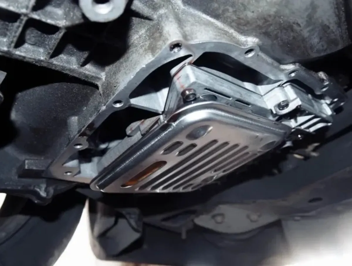 Close-up view of an automatic transmission oil pan with a metallic filter underneath a vehicle.