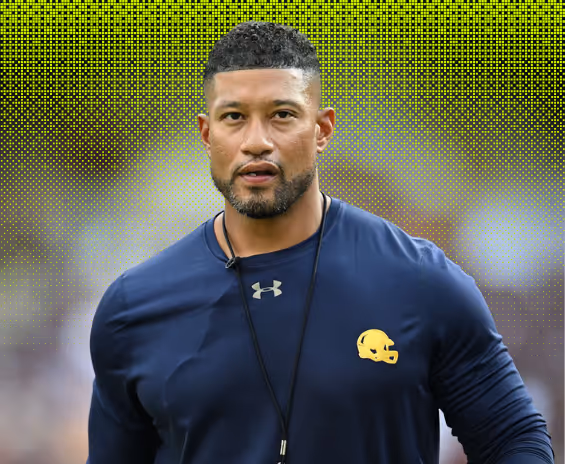 Man wearing a navy blue Under Armour shirt with a yellow football helmet logo and a whistle on a lanyard around his neck.