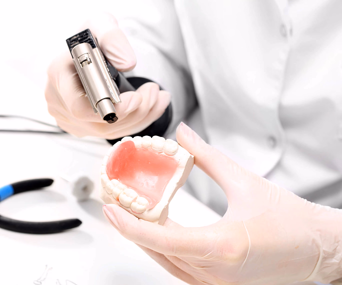 Person wearing gloves holding dental mold and dental tool in a clinical setting.