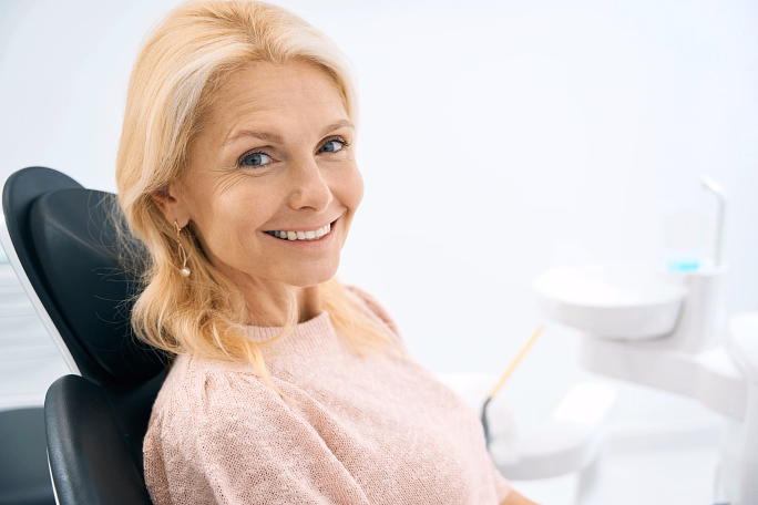Smiling middle-aged woman in a dental chair in a bright dental office.