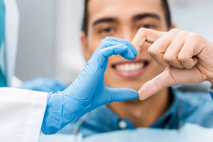 Smiling man and person in medical gloves form a heart shape with hands.