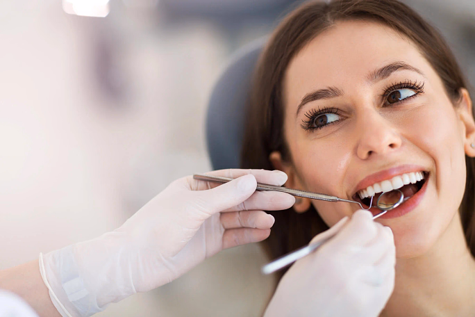 Smiling woman receiving dental checkup with tools from dentist wearing white gloves.