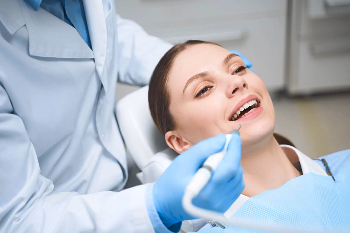 Woman reclining in dental chair with dentist's gloved hand holding dental tool near her mouth.