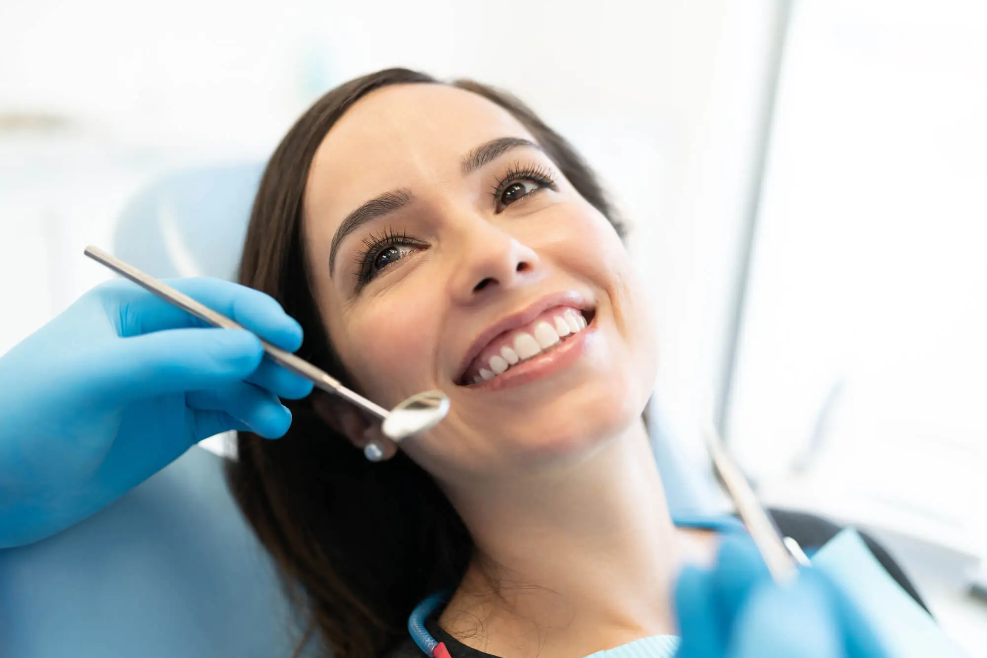 Smiling woman in a dental chair being examined by a dentist wearing blue gloves with dental tools.