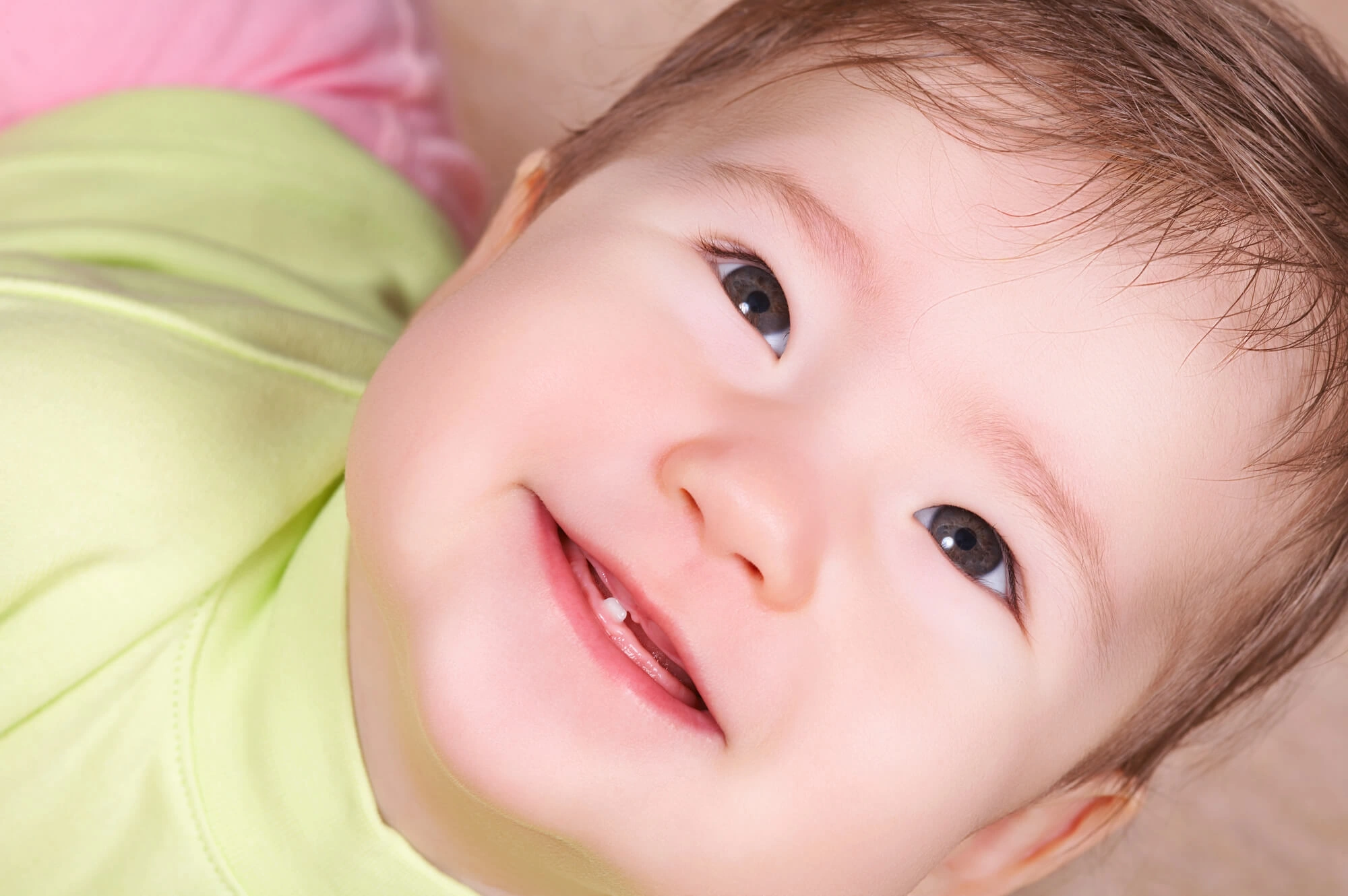 Close-up of a baby smiling, showing emerging front teeth, wearing a light green outfit.