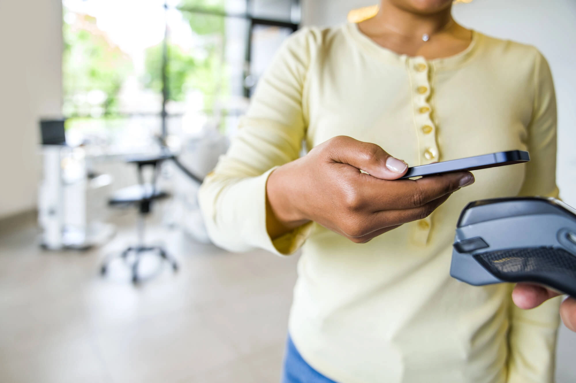 Person holding smartphone near payment terminal to make a contactless payment.