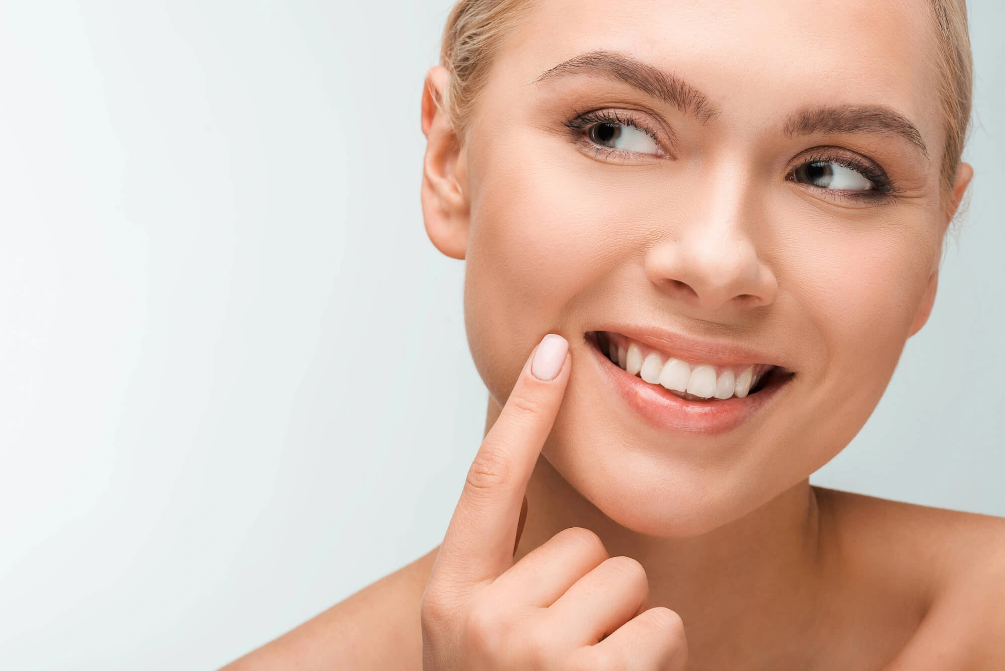 Close-up of a smiling woman pointing to her white, healthy teeth and clear skin.