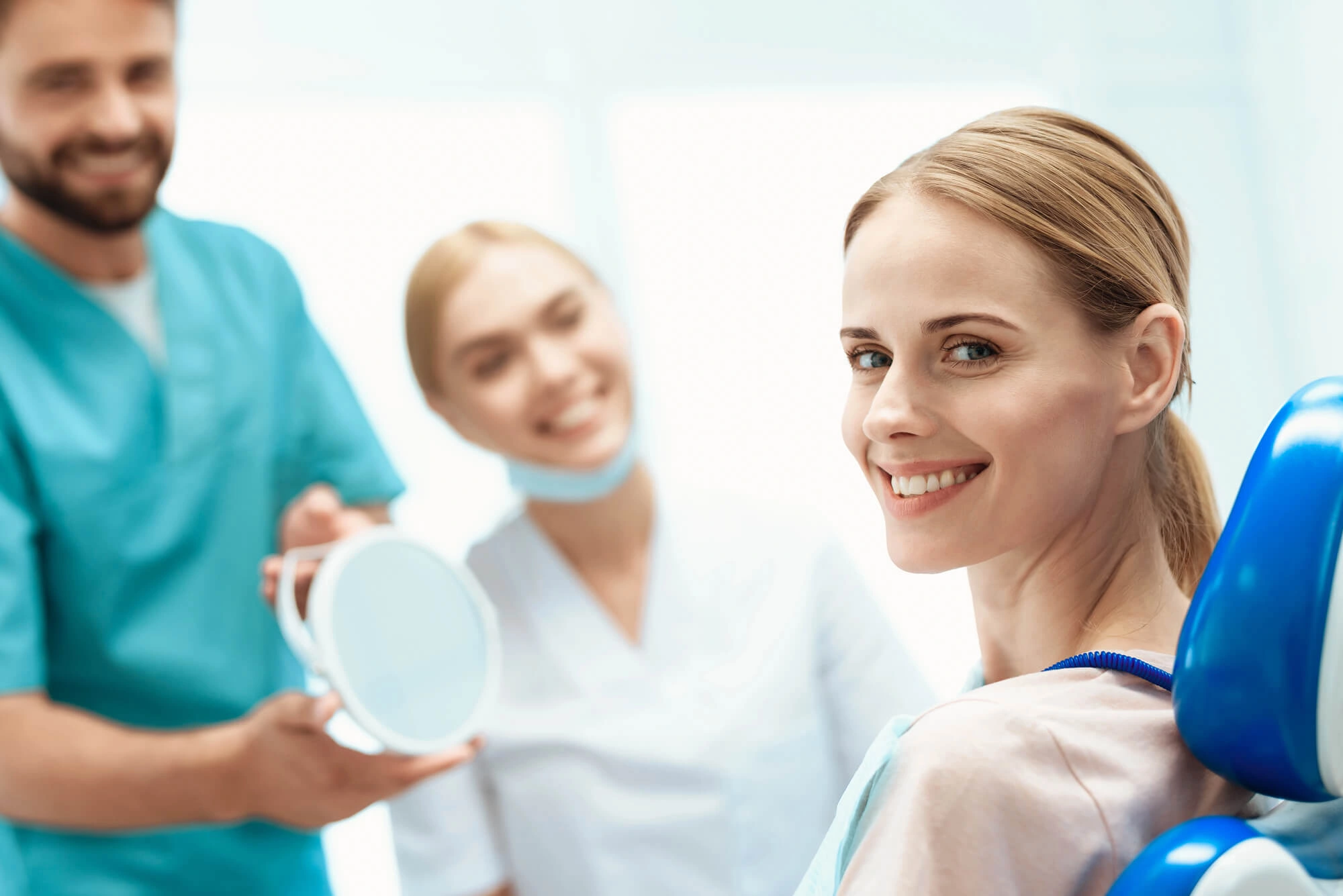 Smiling woman in dental chair with two smiling dental professionals holding a mirror behind her.