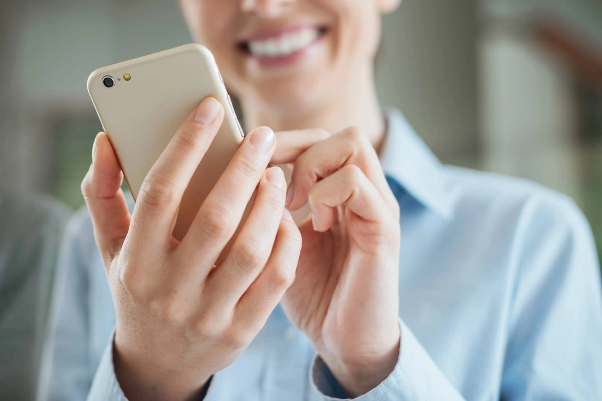 Person smiling while holding and using a gold smartphone with both hands.
