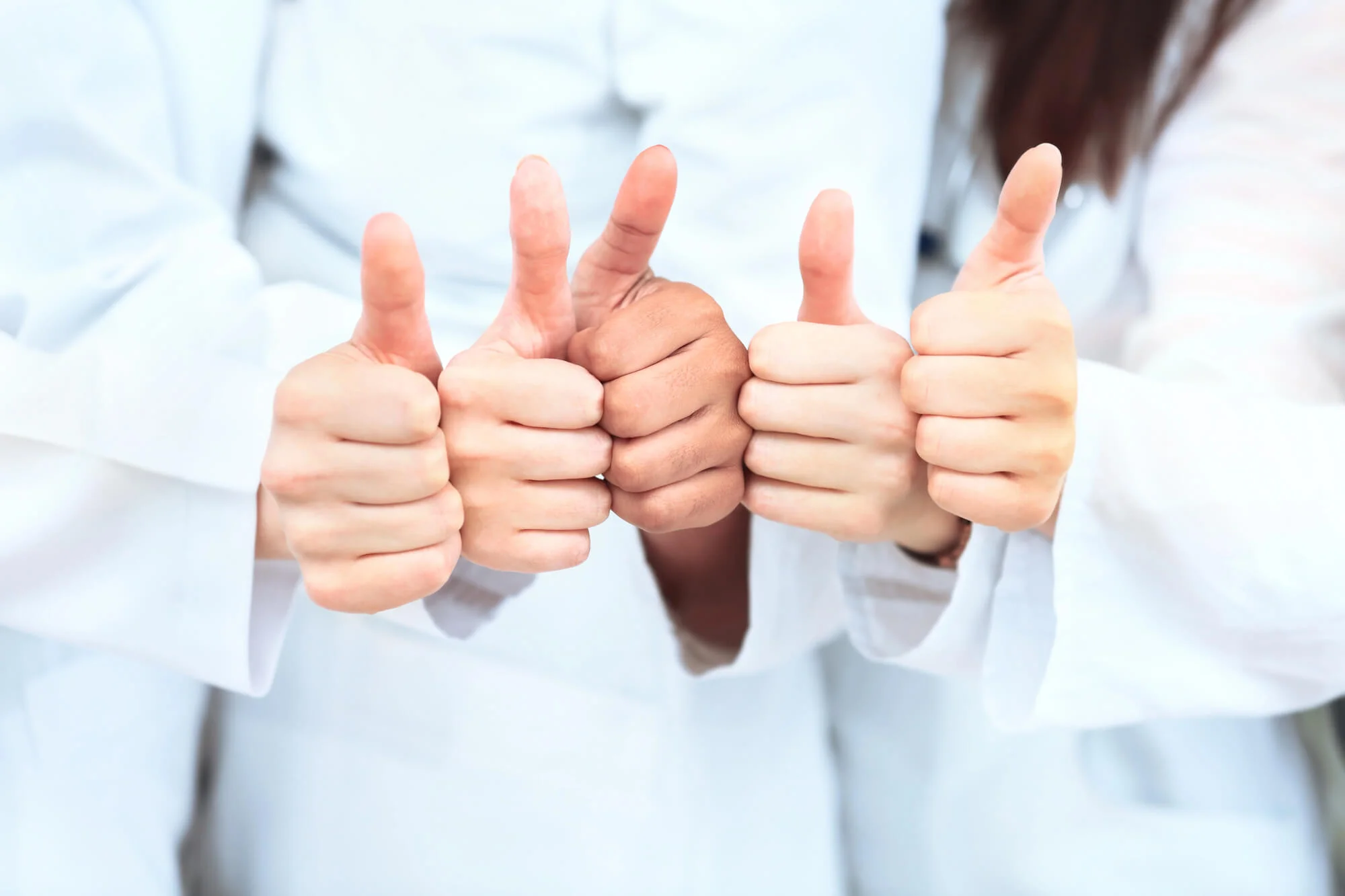 Five diverse hands giving thumbs up, all wearing white sleeves in a row.