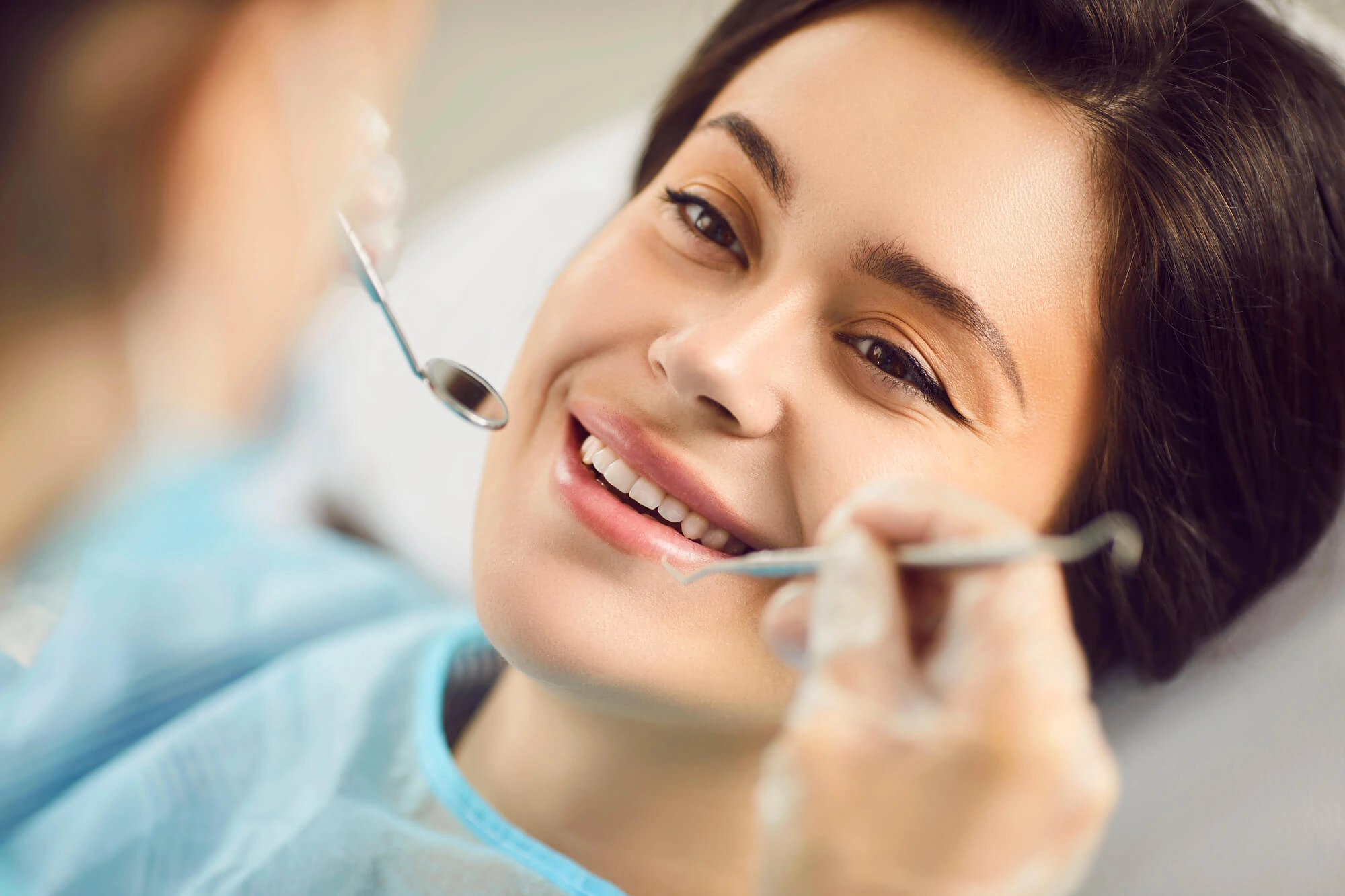 Smiling woman reclined in dental chair with dentist's tools near her mouth during exam.