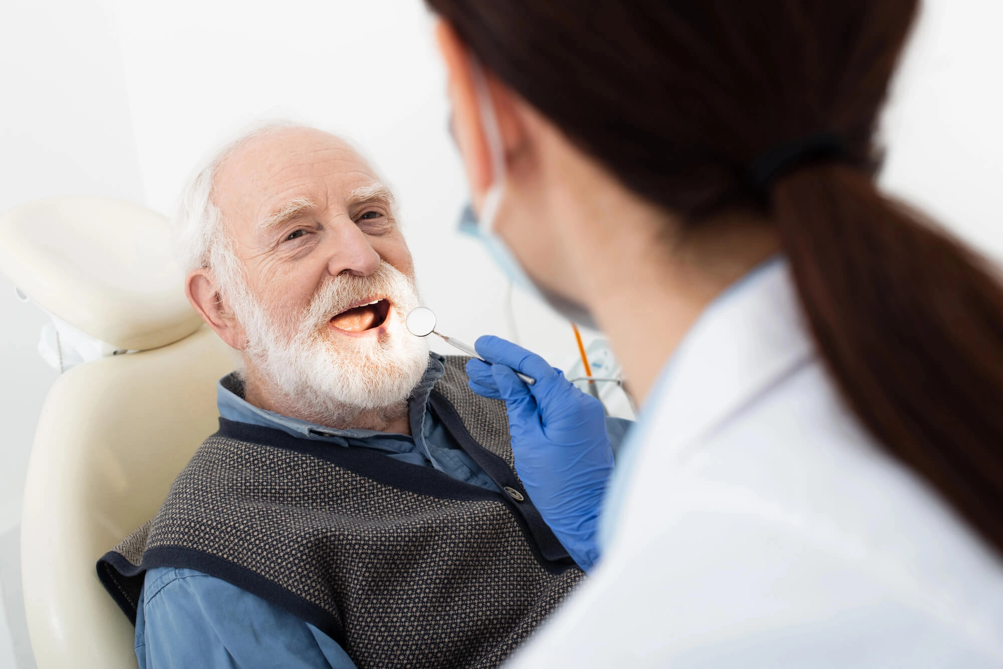 Elderly man in dental chair having his teeth examined by a dentist with blue gloves.
