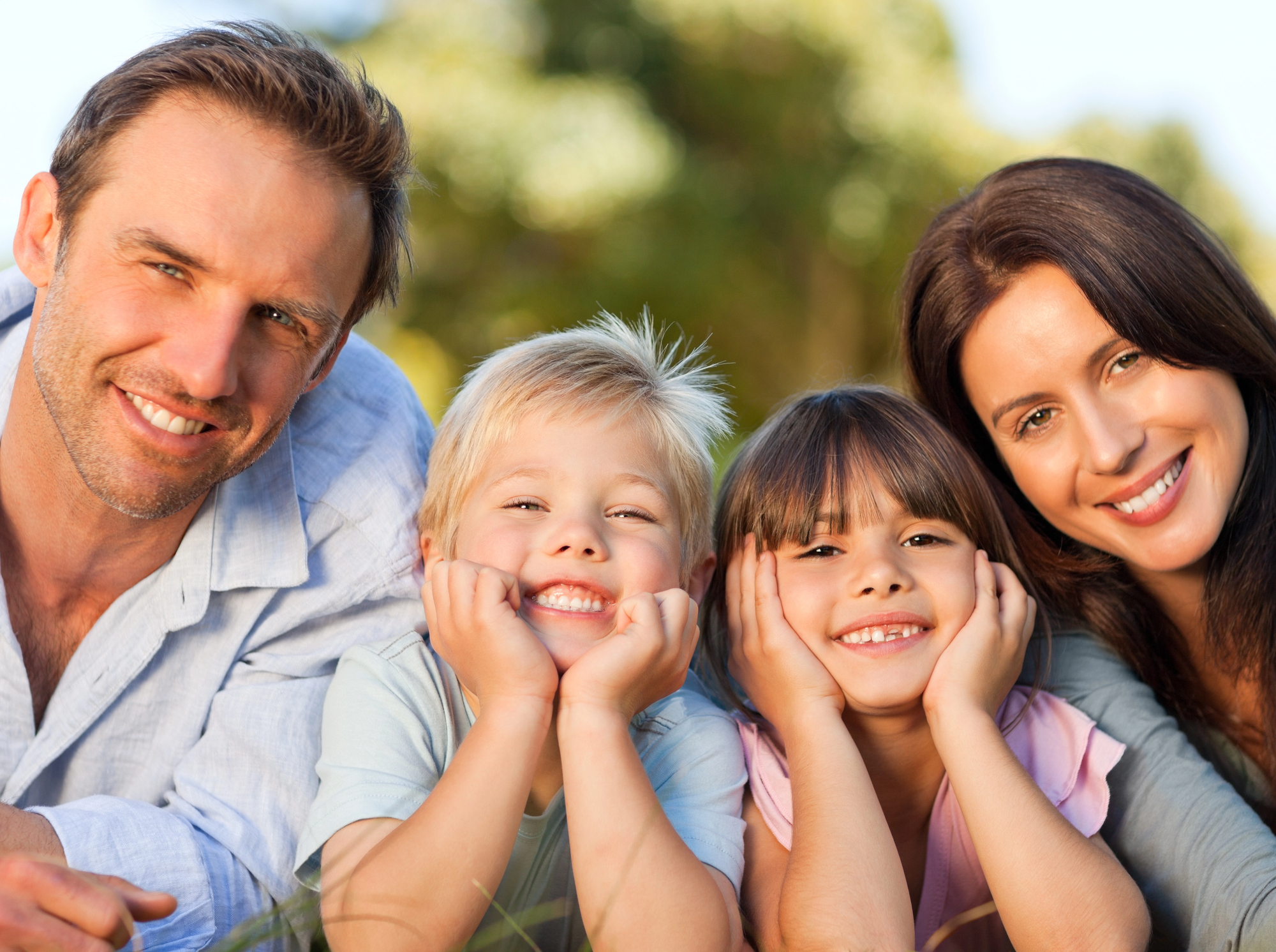 Smiling family of four lying on grass outdoors with father, mother, son, and daughter close together.