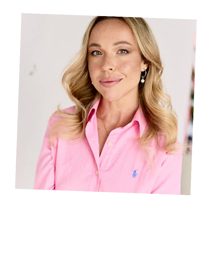Woman with blonde wavy hair wearing a pink button-up shirt and pearl earrings smiling slightly.
