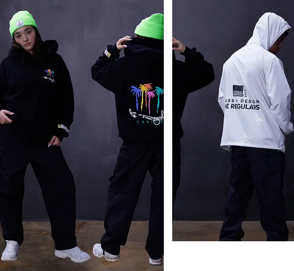 Two models showcasing streetwear: one wearing a black hoodie with colorful palm tree graphics and a neon green beanie, the other in a white hooded jacket with text on the back.