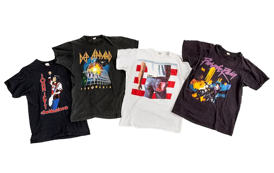 Four vintage rock band T-shirts laid out: Joan Jett, Def Leppard, a white shirt with an image of denim-clad rear and red stripes, and a Prince Purple Rain shirt.