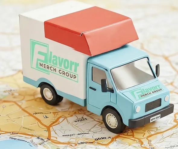 Toy delivery truck with blue cab, white cargo area, and red top, labeled 'Flavorr Merch Group' on a map background.