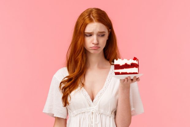 Junge Frau, die traurig ein Stück Kuchen ansieht