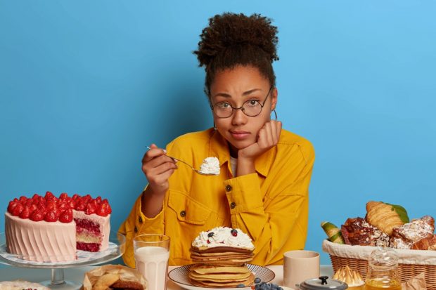 Junge Frau, die traurig vor ungesunden Lebensmitteln sitzt