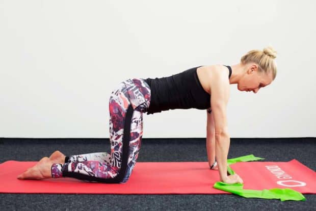 Frau auf roter Trainingsmatte seitlich auf allen Vieren macht Oberkörper Twist mit dem Theraband