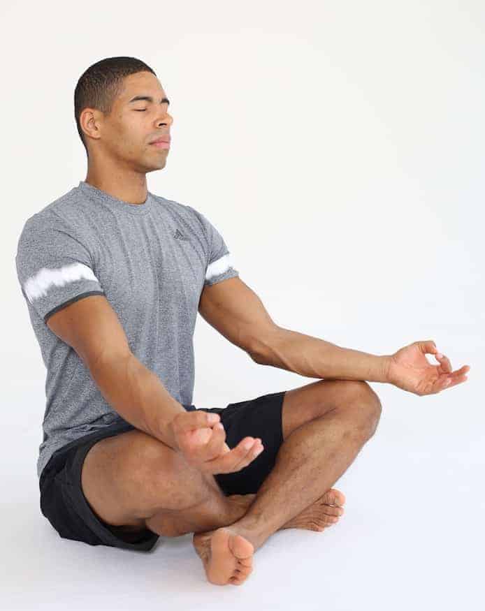 Mann sitzt auf Trainingsmatte in Schneidersitz in Entspannungsposition und macht progressive Muskelrelaxation