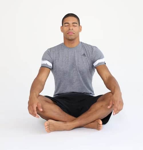 Mann sitzt auf Trainingsmatte in Schneidersitz in Entspannungsposition und macht progressive Muskelrelaxation