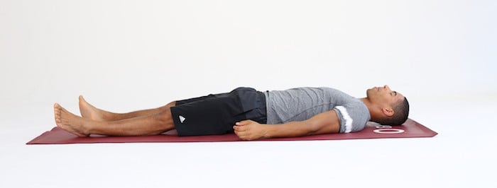 Mann liegt auf Trainingsmatte in Entspannungsposition und macht progressive Muskelrelaxation