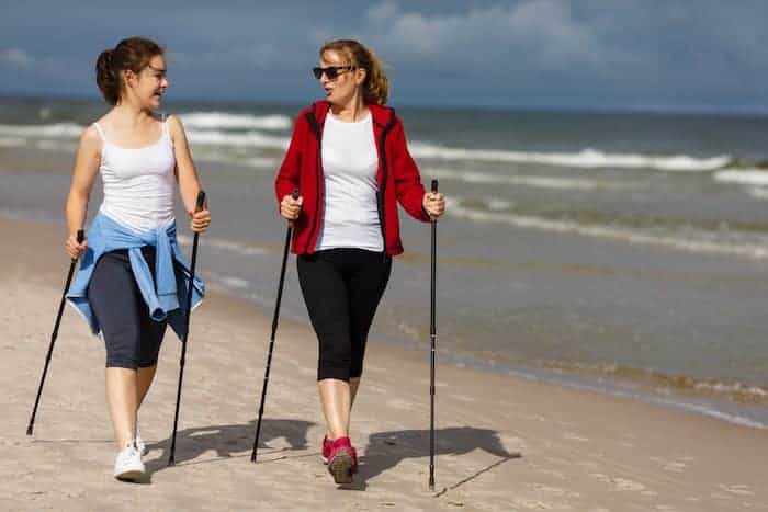 2 Frauen am Strand machenNordic Walking und lächeln sich an