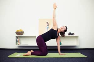 Junge Frau macht Beweglichkeitsübung auf grüner Fitnessmatte