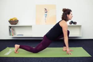 Junge Frau macht Beweglichkeitsübungen auf grüner Matte Lunge & Runners Stretch
