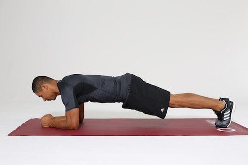 Mann macht Plank auf dunkelroter Trainingsmatte