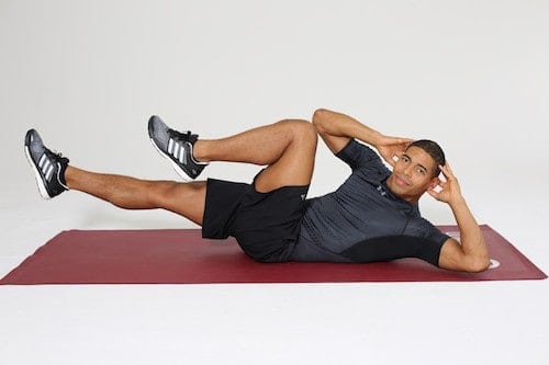 Mann macht Diagonal Crunches auf dunkelroter Trainingsmatte