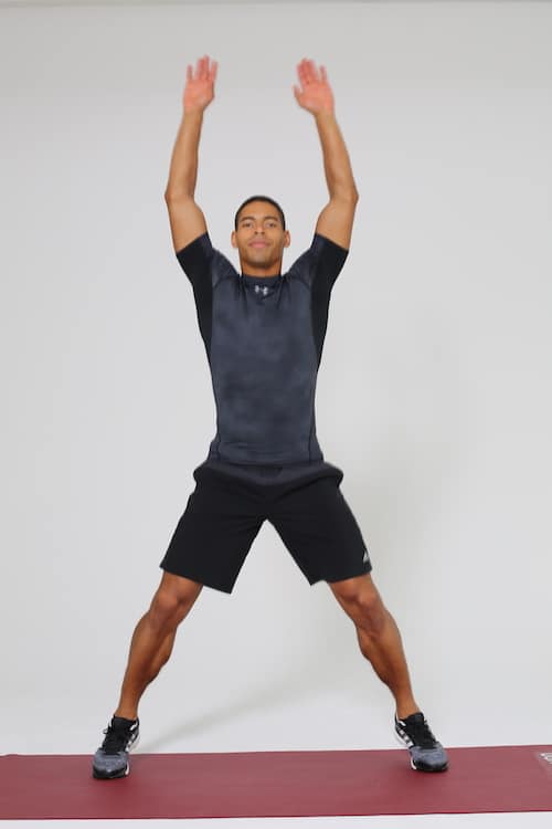 Mann springt Jumping Jacks auf dunkelroter trainingsmatte