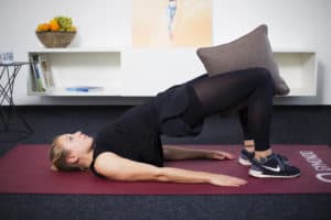 Junge Frau auf Trainingsmatte zu Hause macht Übung für den Beckenboden - Brücke.