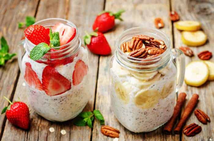 Zwei Gläser mit Overnight Oats, Chia, Erdbeeren, Bananen und Nüssen.