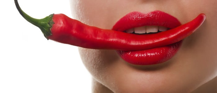 Frau mit Chilischote im Mund mit Lippenstift