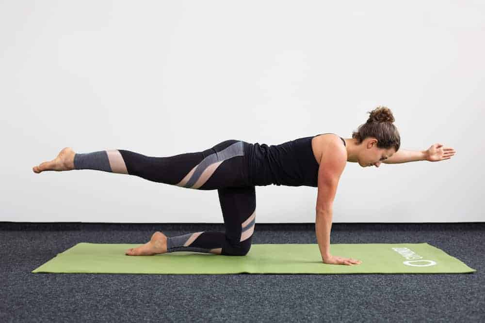Junge Frau auf allen Vieren auf einer hellgrünen Trainingsmatte macht Pilates Quadruped