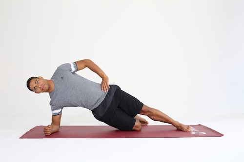 Mann macht Side Plank auf dunkelroter Trainingsmatte