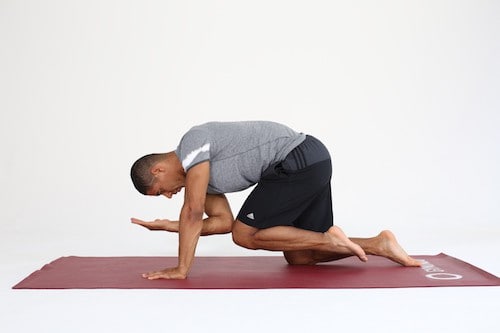 Mann macht Rückenübung auf allen Vieren All Fours auf dunkelroter Trainingsmatte