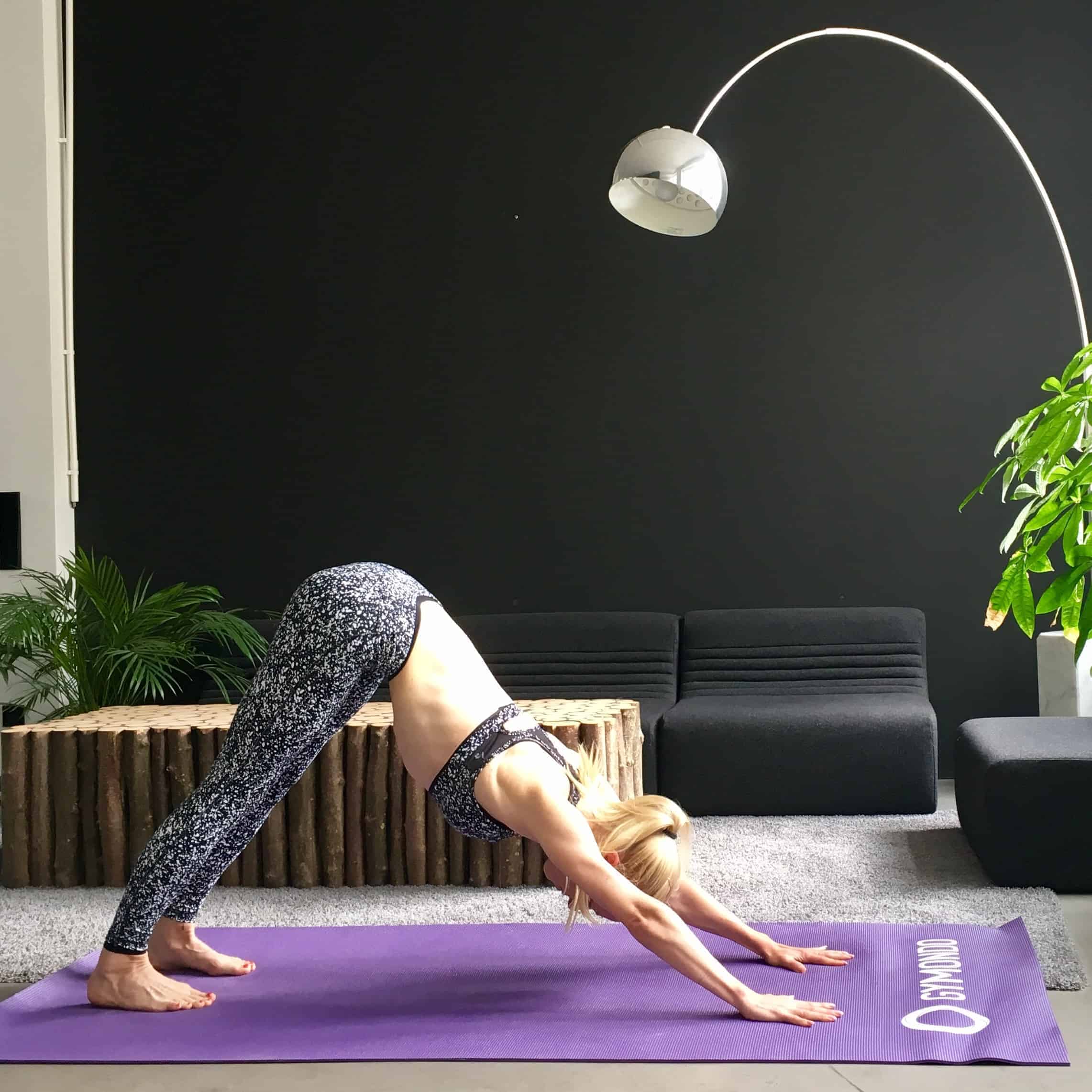 Frau macht Yoga Sonnengruß Down Dog auf lila trainingsmatte