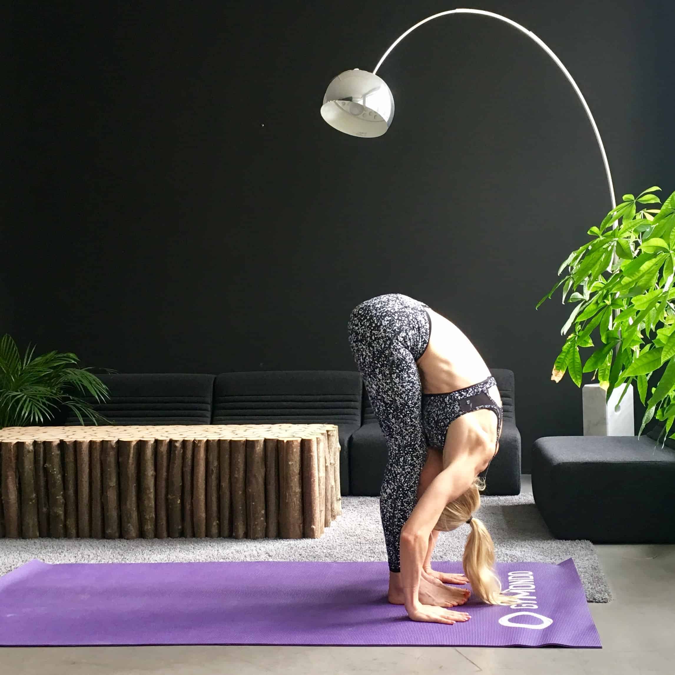 Frau macht Yoga Sonnengruß Vorbeuge auf lila trainingsmatte