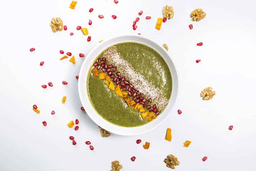 weiße Schale mit grünem Frühstücksbrei garniert Gojibeeren und Walnüssen 