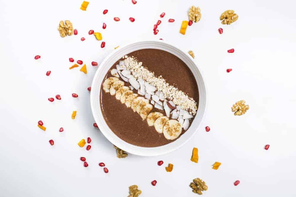 Weiße Schale mit Schokoladen Frühstücksbrei garniert mit Bananenscheiben und gehobelten Mandeln