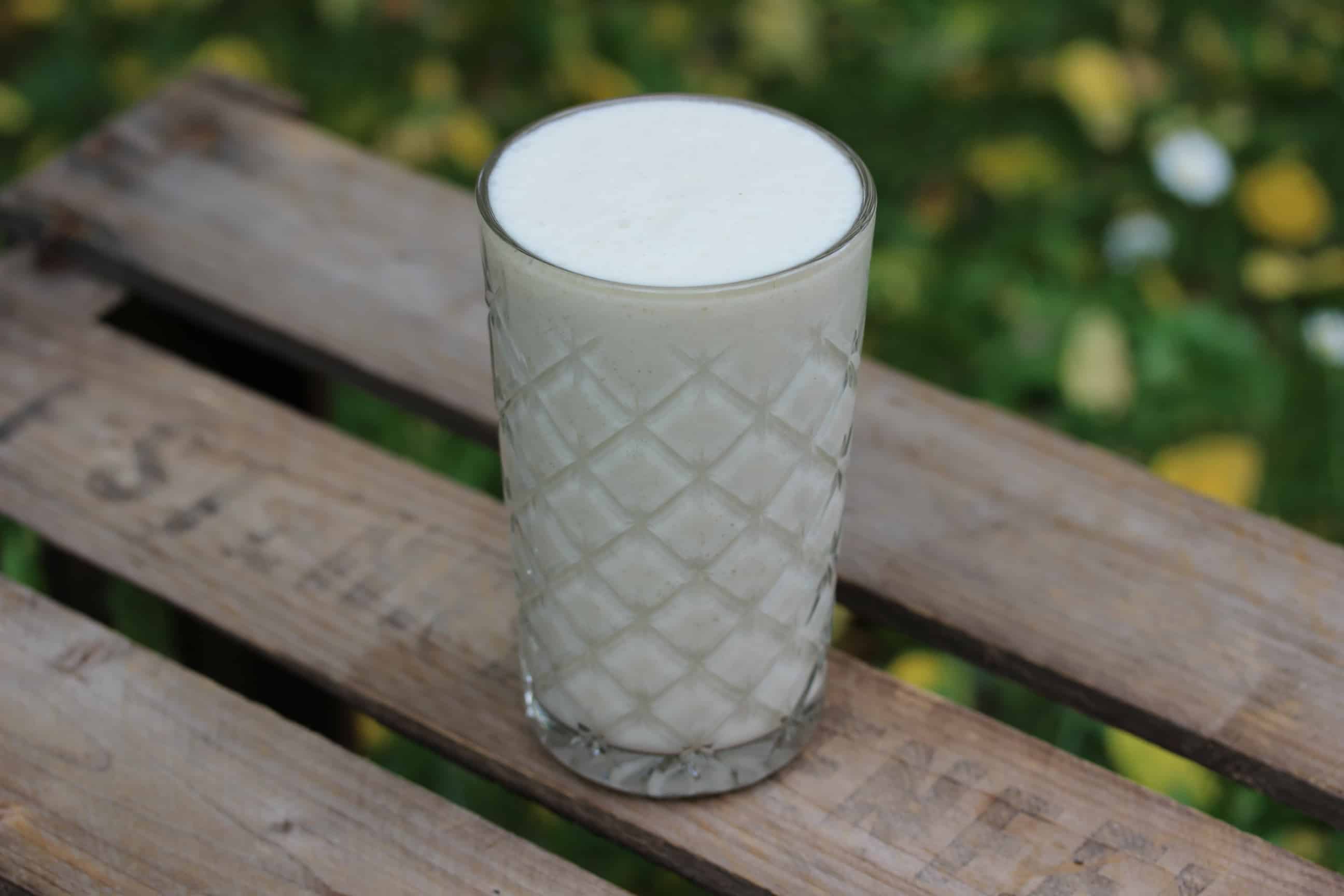 SuperGoodFood SuperClean Banana „Milk“ in Glas auf Holztisch