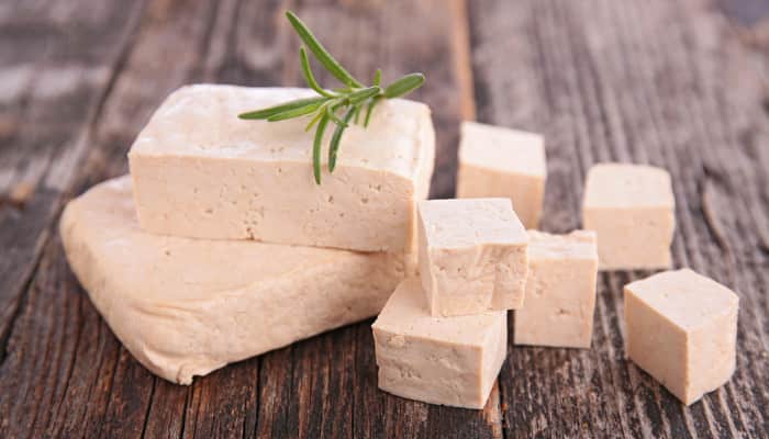 Tofu, gewürfelt und in Scheiben auf einem Holztisch, garniert mit einem grünen Zweig