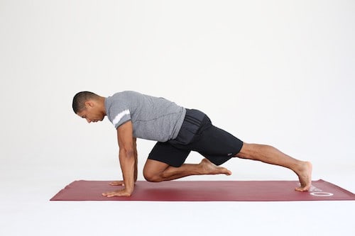 Mann macht Mountain Climbers auf dunkelroter Trainingsmatte - Plank Varianten